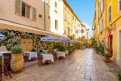 A picturesque alley of shops and sidewalk cafes in the colorful old town section of the Mediterranean resort city of Saint-Tropez, France, along the French Riviera.