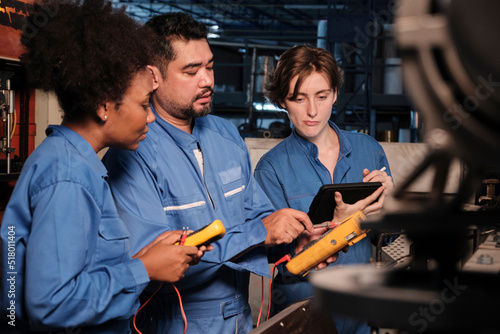Multiracial professional industry engineer teams in safety uniforms work by inspecting machines' voltage current, checking, and maintaining at manufacture factory, electric system service occupations.