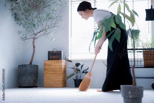明るい植物の部屋でほうきで掃除する日本人女性