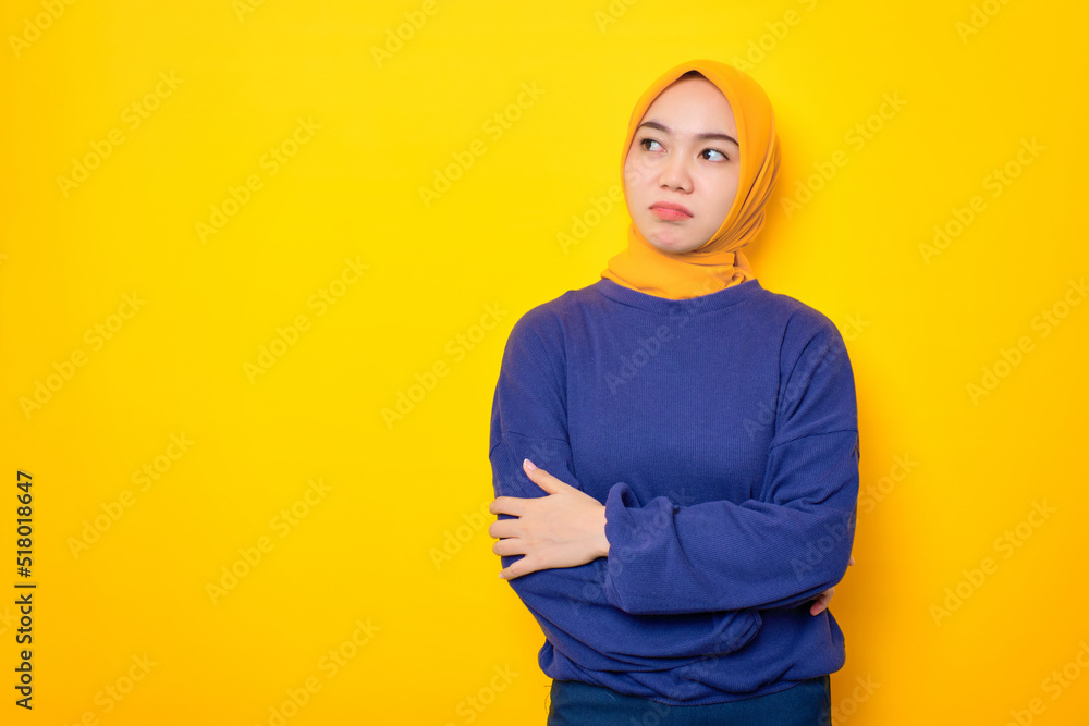 Pensive young Asian Muslim woman dressed in casual sweater looking up at copy space and touching chin, thinking about interesting offer isolated over yellow background Pensive young Asian Muslim woman dressed in casual sweater looking up at copy space and touching chin, thinking about interesting offer isolated over yellow background
