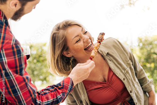 Fototapeta A young curvy woman laughs as she eats skewers of meat from her friend's hands during a trip to the countryside