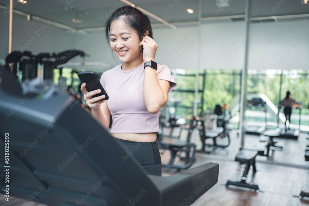 Fototapeta premium Portrait of an Asian woman exercising on a treadmill She is listening to music with wireless headphones and a smart watch.