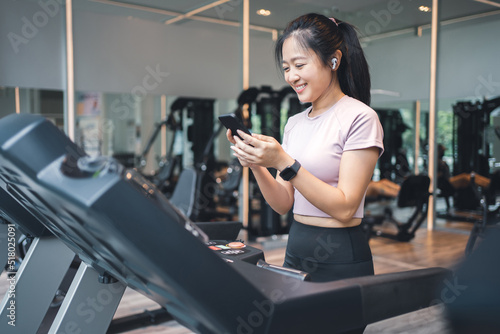Young woman exercises on a treadmill and she is using a smartphone in the gym.
