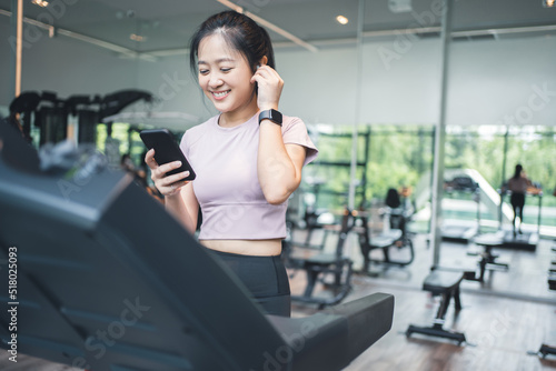 Portrait of an Asian woman exercising on a treadmill She is listening to music with wireless headphones and a smart watch.