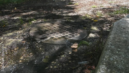 Sewage flows from under the metal cover of the sewer manhole in the park.