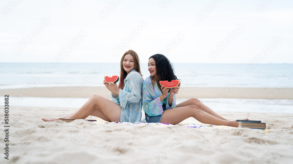 two girls sitting on a laptop and reading books and holding fruit on vacation holiday concept travel lgbtq