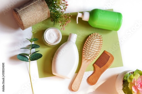 Toiletries kit, natural bath products flat lay photography. White shampoo bottle, facial cream, wooden hair brushes, liquid soap and plants on a green background