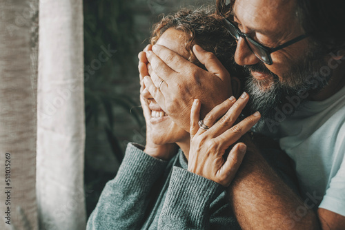 Couple at home in romance leisure activity. Man covering eyes to woman making a surprise. People in love and relationship indoor. Happy lady with husband enjoying a new day. Serene married people photo