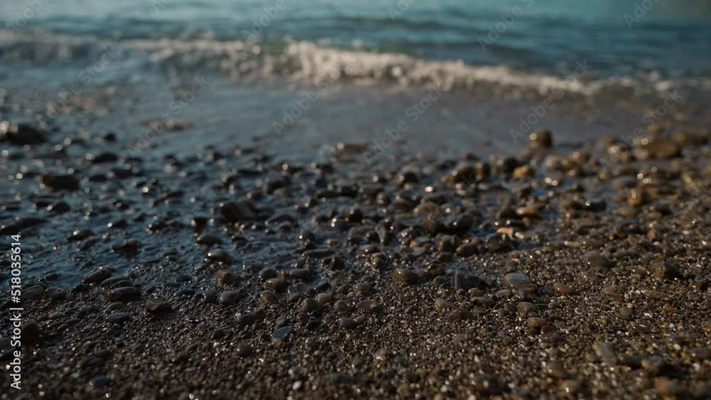 close up slow motion ocean sea waves rolls on shore of pebble beach at afternoon. sun flares on water and wet pebbles. selective focus, summer vibe, nature beauty close up slow motion ocean sea waves rolls on shore of pebble beach at afternoon. sun flares on water and wet pebbles. selective focus, summer vibe, nature beauty