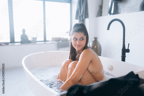 Young woman hugs her legs while sitting in the bath photo