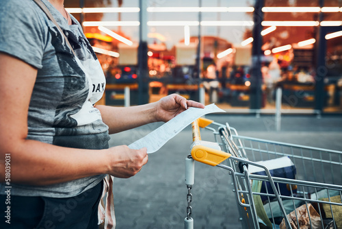 Woman looking at higher prices on receipt after shopping in grocery store. Increasing prices caused by inflation. Higher bills. Economic crisis