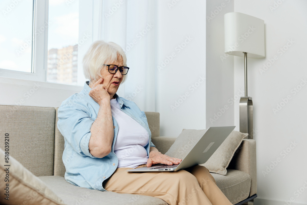 sad nice lady is sitting on the couch holding a laptop on her lap looking at the camera sad nice lady is sitting on the couch holding a laptop on her lap looking at the camera