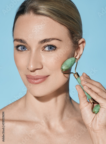 Face jade roller. Face of beautiful woman with green jade roller for anti-aging procedures