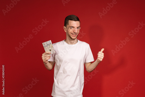 A young man in a white T-shirt with Treacher Syndrome is holding a passport photo