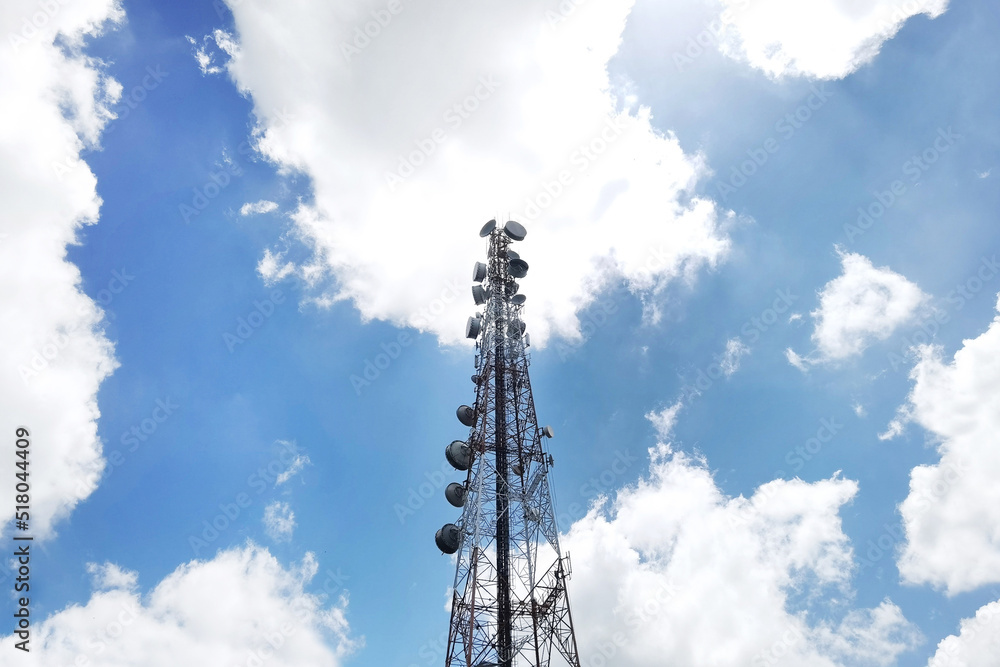 Red and white tower of communications with a lot of different antennas under blue sky and clouds Red and white tower of communications with a lot of different antennas under blue sky and clouds