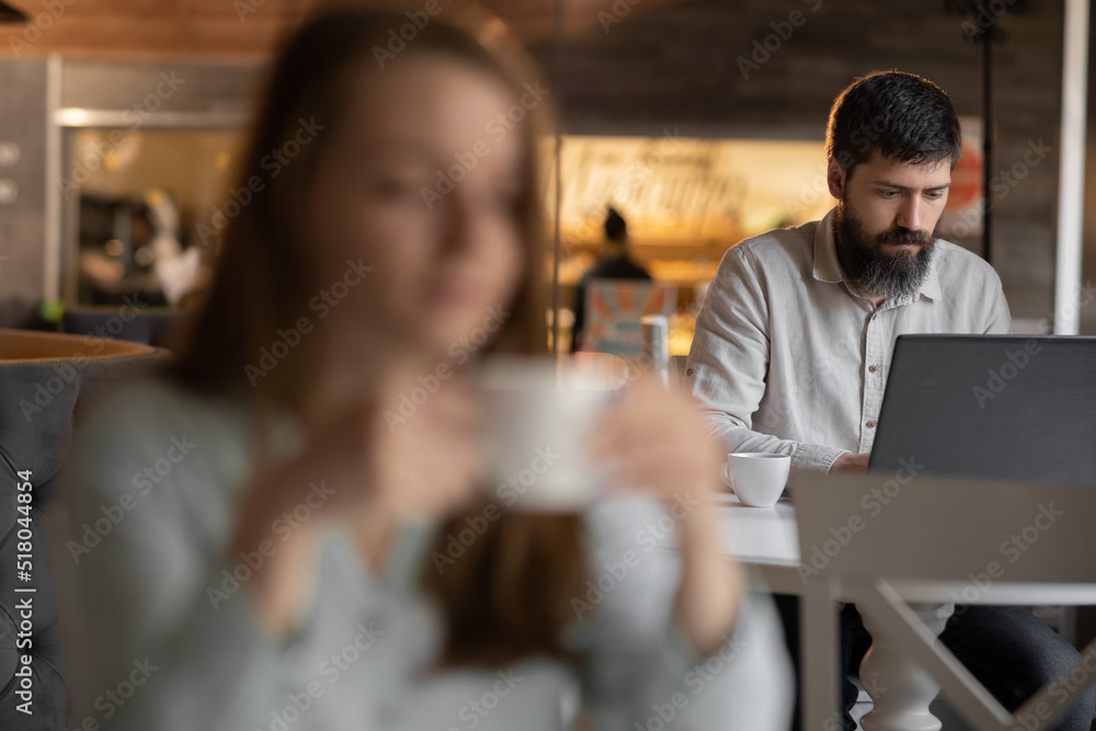 successful business man sitting at the cafe working on a laptop, girl is blurred on foreground, work of freelancer successful business man sitting at the cafe working on a laptop, girl is blurred on foreground, work of freelancer
