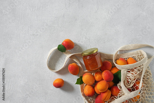 apricots in string bag and jar with apricot jam on white table. copy space. top view