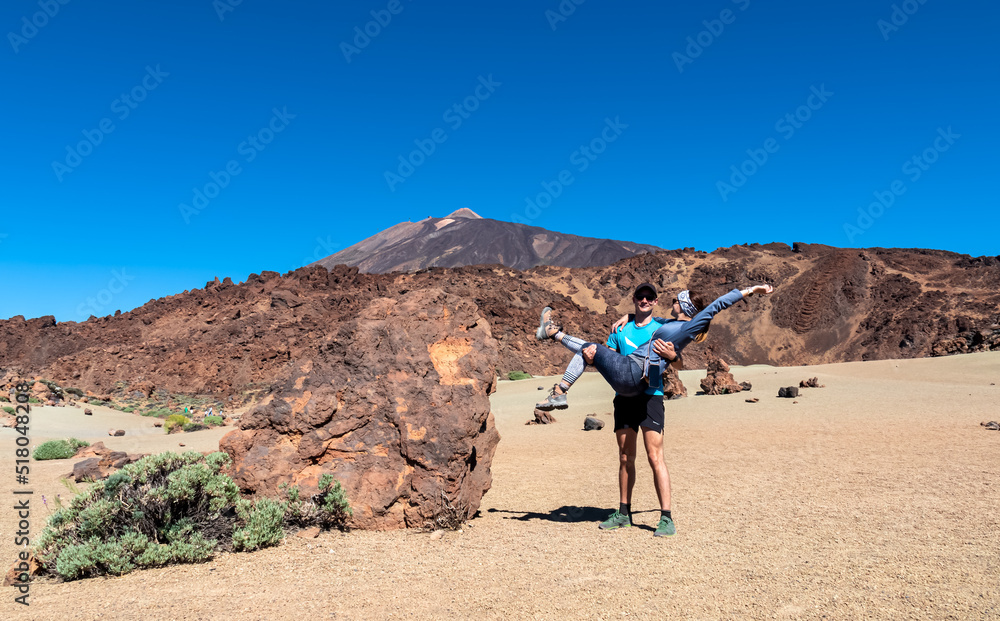 Couple with scenic view on moon landscape of Minas de San Jose Sur near volcano Pico del Teide, Mount El Teide National Park, Tenerife, Canary Islands, Spain, Europe. Man carrying woman. Lava rock