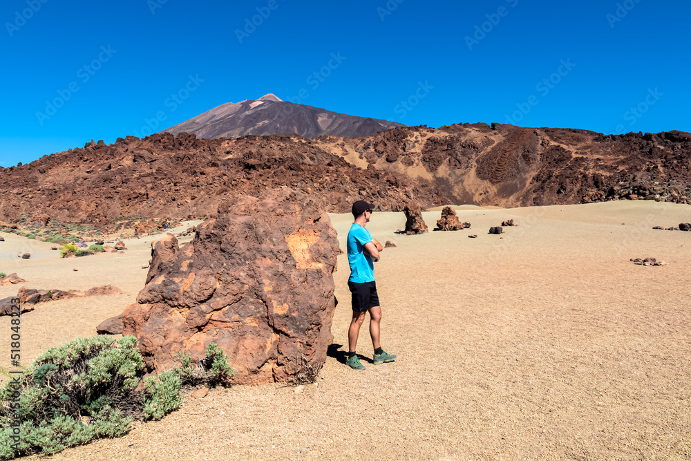 Rear view of hiking man with scenic view on moon landscape of Minas de San Jose Sur near volcano Pico del Teide, Mount El Teide National Park, Tenerife, Canary Islands, Spain, Europe. Lava rocks