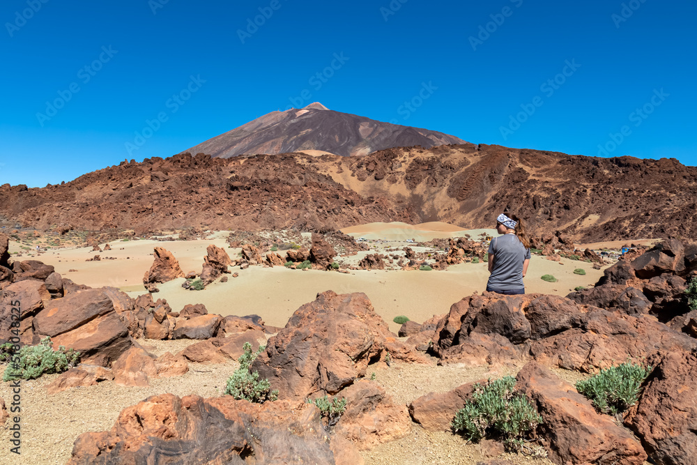 Naklejka premium Rear view of hiking woman sitting on lava rock. Scenic view on moon landscape Minas de San Jose Sur near volcano Pico del Teide, Mount El Teide National Park, Tenerife, Canary Islands, Spain, Europe