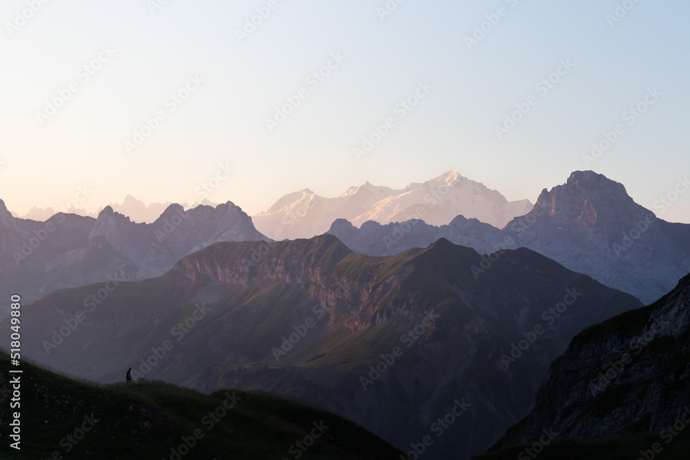 Mont Blanc mountains at sunrise in French Alps from the Lake of Peyre. Man silhouette staring at the vastness of the mountains surrounding him
