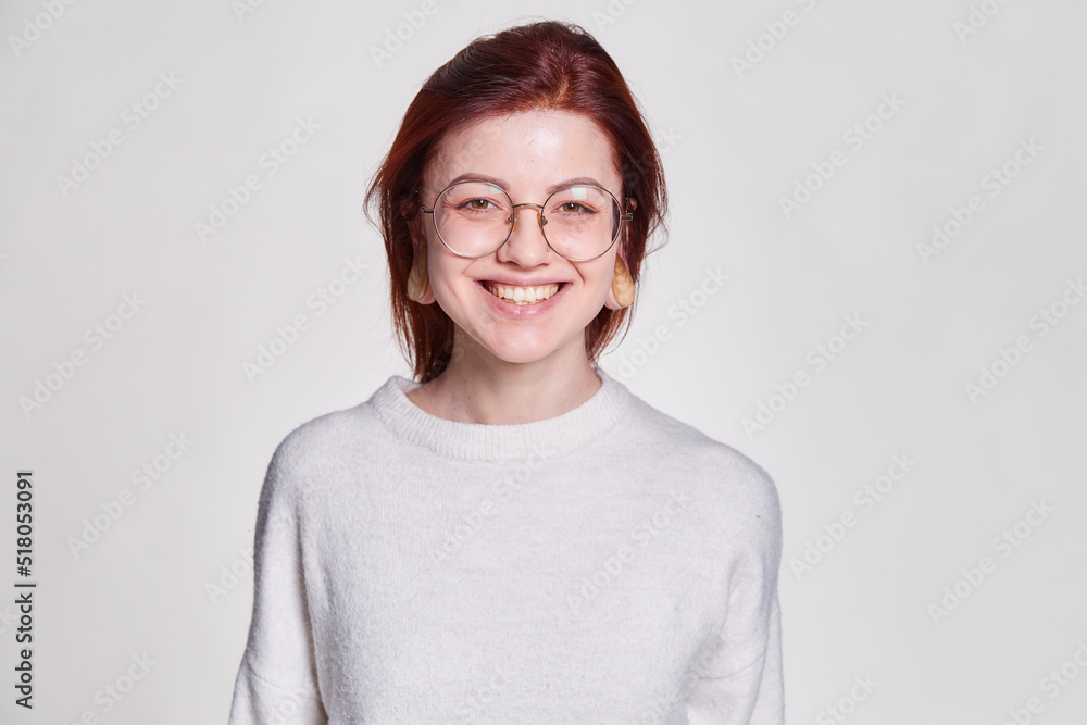 Smiling redhead woman in big eyeglasses with pierced tunnel in ears posing over white background copy space Smiling redhead woman in big eyeglasses with pierced tunnel in ears posing over white background copy space