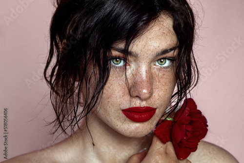 beauty young woman face with a lot of freckles and red lips, red rose near face, close up