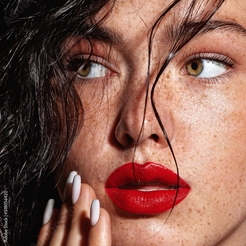 beauty young woman face with a lot of freckles and red lips, hand near face, close up
