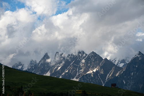 Clouds over the mountains. Amazing high rocks in the fog with green hills . © Inga Av
