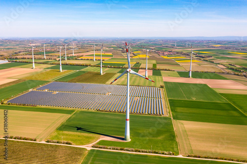 Panorama von Solarmodulen eines Solarparks als Freiflächenanlage inmitten von Windrädern zwischen landwirtschaftlichen Feldern in Deutschland