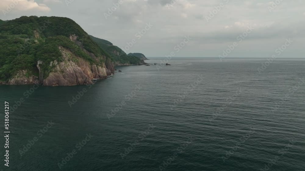 Slow move over calm sea towards steep cliffs and rugged coast at dawn