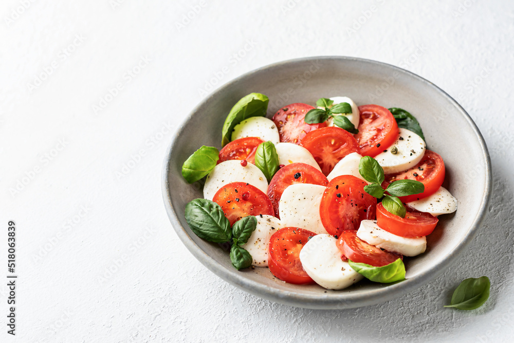 Caprese salad with tomatoes mozzarella basil and olive oil with a basil leaf near on white background. Text space