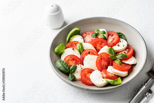 Caprese salad with tomatoes mozzarella basil and olive oil on white background served with cutlery and salt shaker. Text space