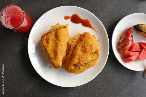 Rustic homemade Bread Pakora or triangle shape pakoda served with tomato ketchup on a brekfast table along with watermelon juice, fruits and tea. Indian tea-time snack. Copy space
 photo