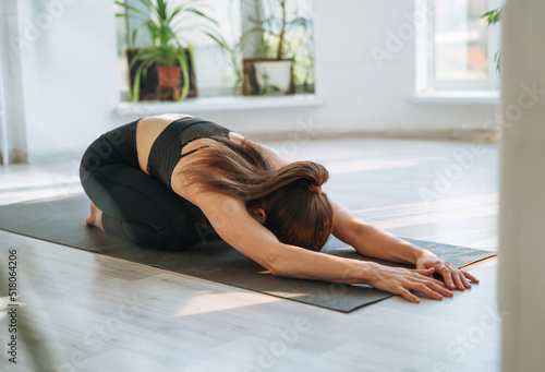 Young fit woman practice yoga doing asana in light yoga studio with green house plant