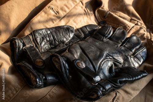 Short black leather motorcycle gloves on a tan jacket. Retro Biker gloves from the 1950's. Stylish and retro short black leather biker gloves on a tan jacket. Shadow and warm colors.
