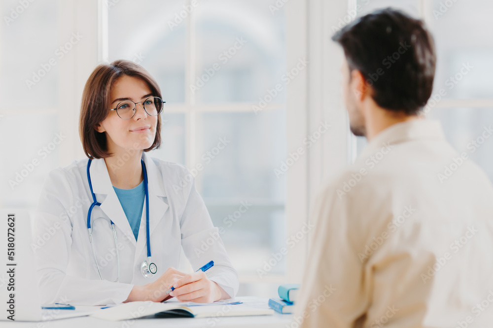 Heathcare, therapy session and assistance concept. Professional woman doctor speaks with male patient, gives consultancy and makes prescription, finds out symptoms of disease, provides help. Heathcare, therapy session and assistance concept. Professional woman doctor speaks with male patient, gives consultancy and makes prescription, finds out symptoms of disease, provides help.