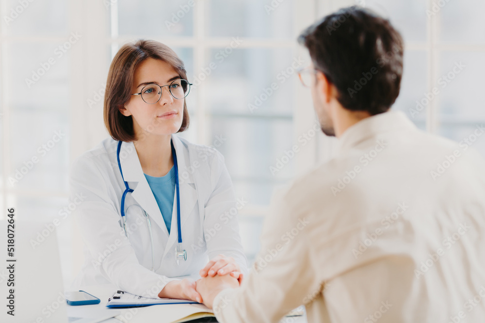 Friendly female doctor tries to support patient, holds his hands, gives useful consultation and explains medical information, makes diagnostic examining, pose in hospital room. Heathcare, assistance Friendly female doctor tries to support patient, holds his hands, gives useful consultation and explains medical information, makes diagnostic examining, pose in hospital room. Heathcare, assistance