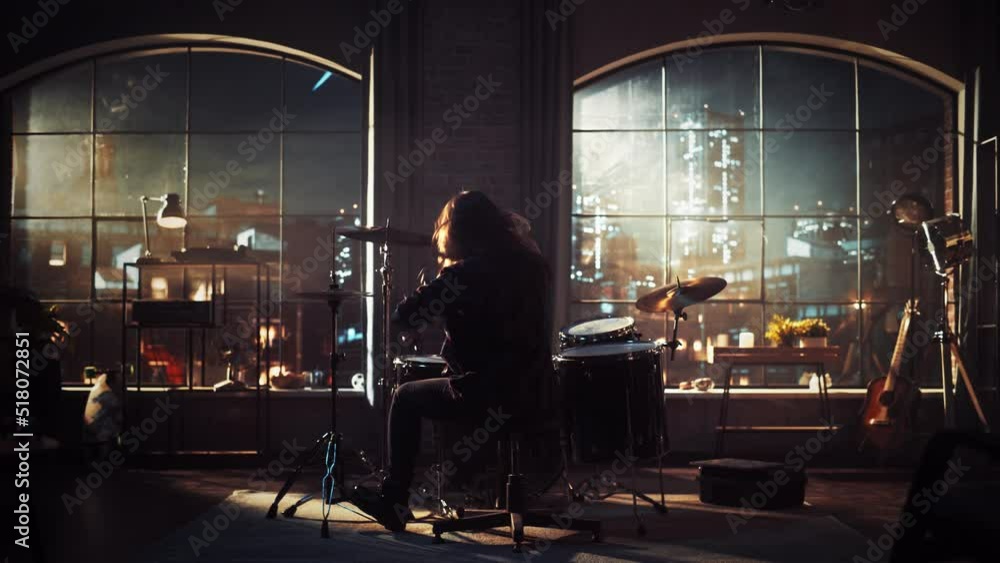 Person Sitting with Their Back to Camera, Playing Drums During Rehearsal in a Loft Studio with Sunlight. Drummer Practising Alone Before a Live Concert on Stage. Evening or Night Session. Static Shot. Person Sitting with Their Back to Camera, Playing Drums During Rehearsal in a Loft Studio with Sunlight. Drummer Practising Alone Before a Live Concert on Stage. Evening or Night Session. Static Shot.
