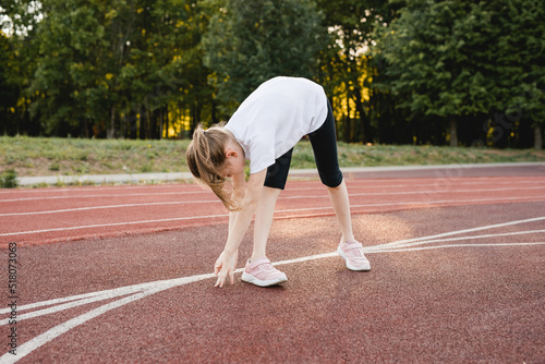 Child girl stretching on a sports track before running