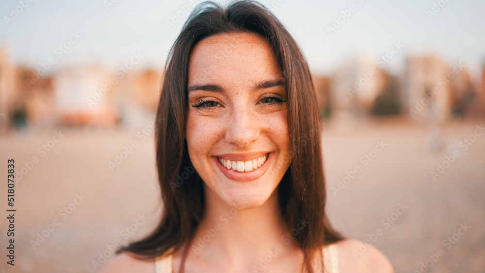 Beautiful brown-haired woman with long hair sits on the beach. Gorgeous girl with freckles and long eyelashes looks at the camera. Beautiful brown-haired woman with long hair sits on the beach. Gorgeous girl with freckles and long eyelashes looks at the camera.