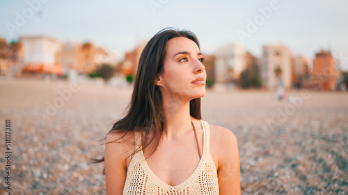 Beautiful brown-haired woman with long hair sits on the beach.