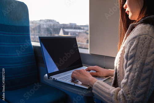 Asian woman working on laptop on train next to the window.