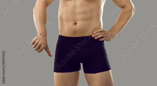 Guy in underwear showing thumbs down standing isolated on grey background. Young male has trouble with intimate matters. Man has difficulty getting erection. Erectile dysfunction and impotence concept