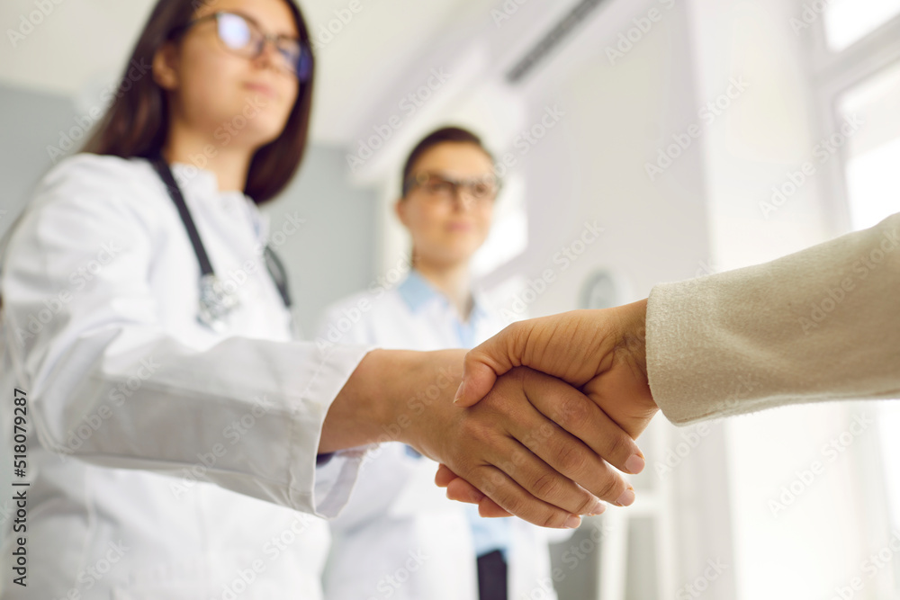 Fototapeta premium Close up hand shake woman doctor and patient symbolizing saving life of diseased in hospital and gratitude to medical system or business agreement with pharmaceutical company . Selective focus