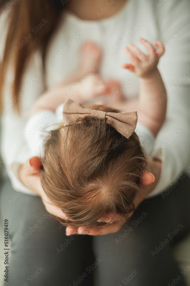 Naklejka premium Close portrait of a little cute dark-haired newborn girl in a white suit in the arms of a young mother. Motherhood. Parent. Healthy sleep.
