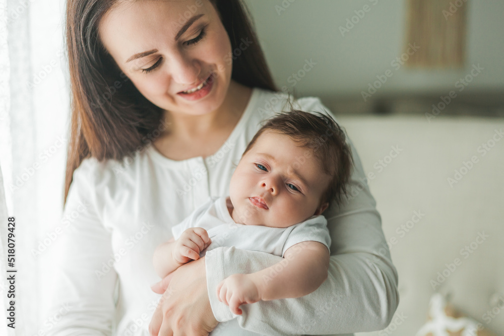 Close portrait of a little cute dark-haired newborn girl in a white suit in the arms of a young mother. Motherhood. Parent. Healthy sleep. Close portrait of a little cute dark-haired newborn girl in a white suit in the arms of a young mother. Motherhood. Parent. Healthy sleep.