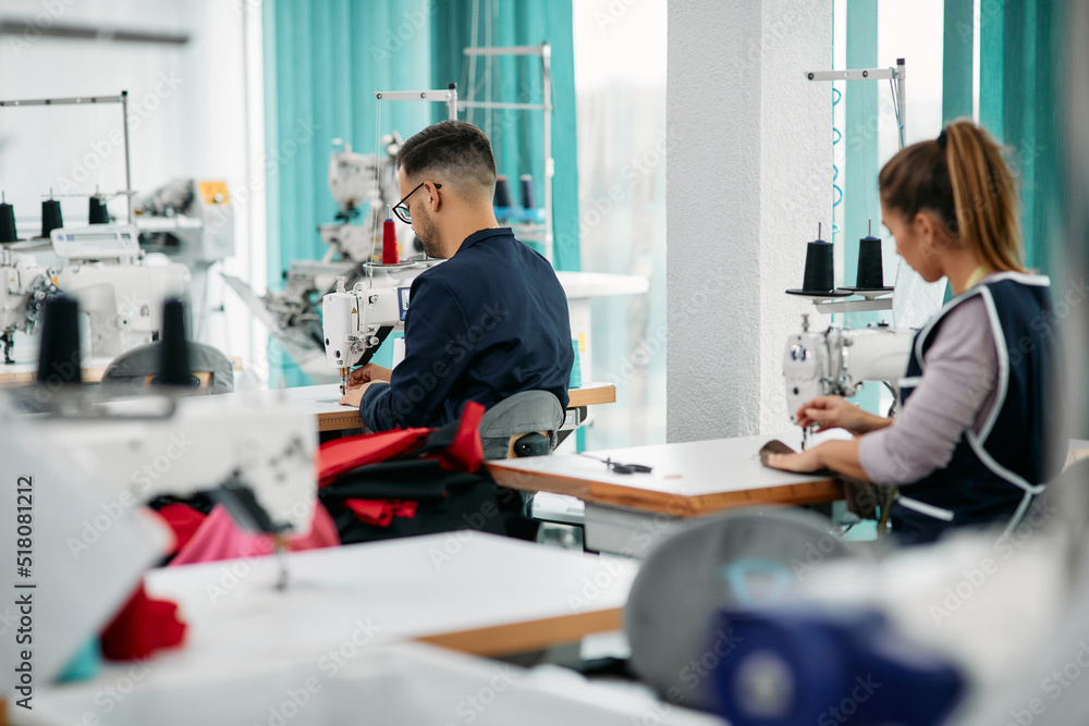 Obraz premium Rear view of textile workers sewing at production line in factory.