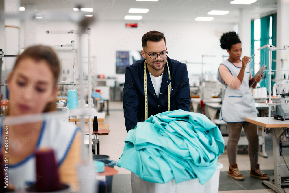 Obraz premium Young tailor pushing cart with materials through textile factory.