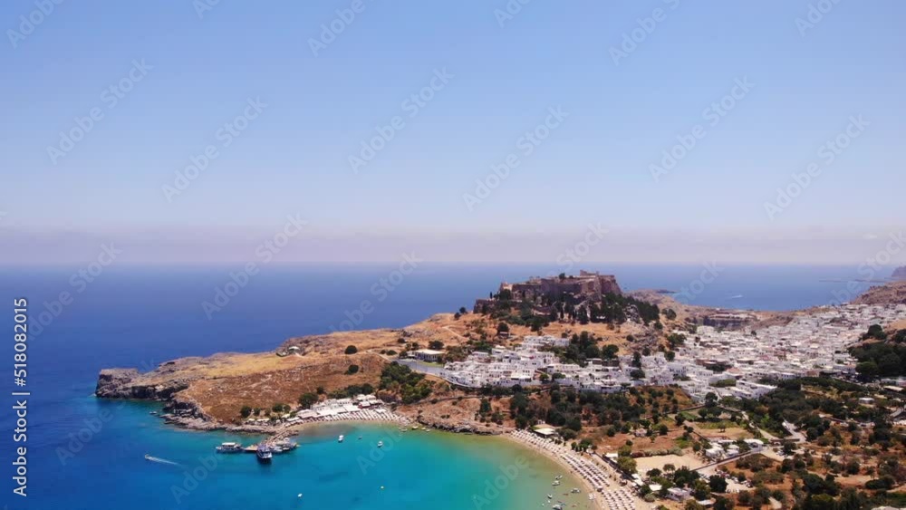 Aerial View Of Lindos Beach, White Houses Of Village And Acropolis In Background, Rhodes, Greece - drone shot Aerial View Of Lindos Beach, White Houses Of Village And Acropolis In Background, Rhodes, Greece - drone shot